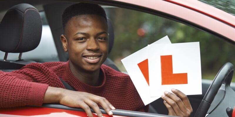 Boy holding up l-plates through drivers side window