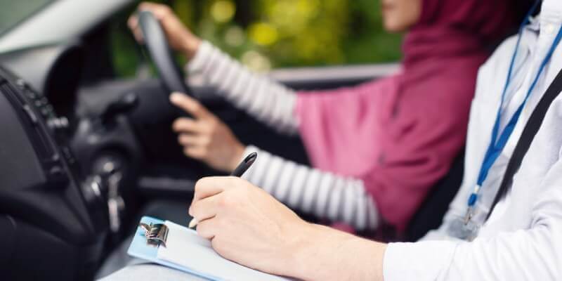 Girl driving while examiners hand writes on the driving test sheet