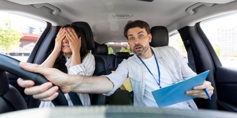 Instructor leaning over to grab the steering wheel in the car