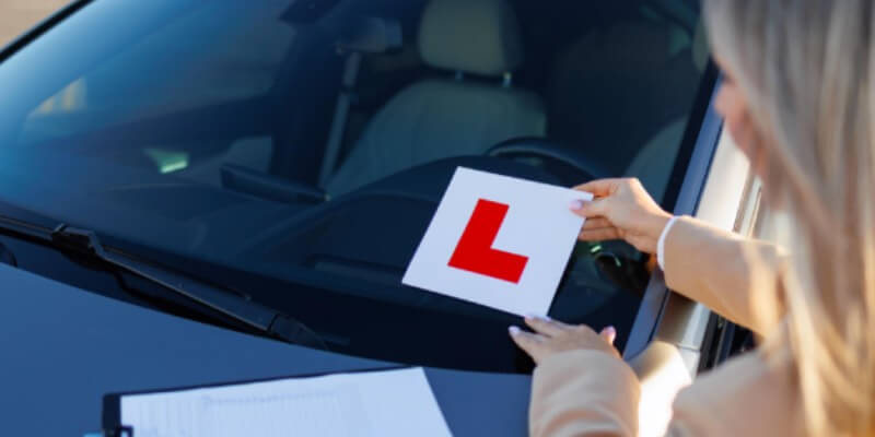 Woman placing l-plate sticker onto the windscreen of a car